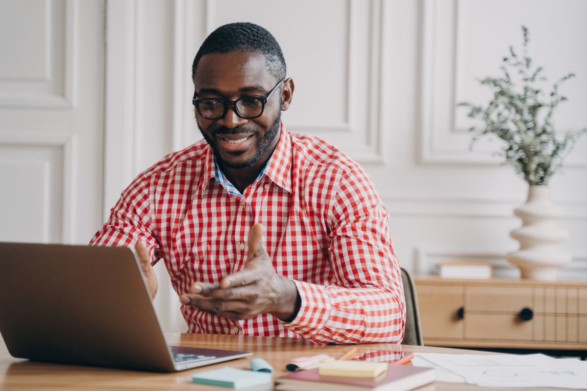 Positive african man online teacher tutor looking at laptop